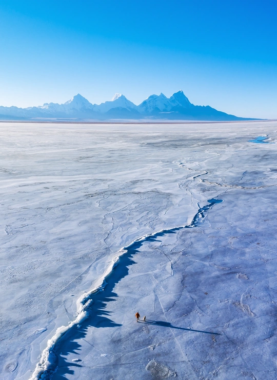沙漠中一座被冰封的湖上的冰裂缝 背景是山脉。