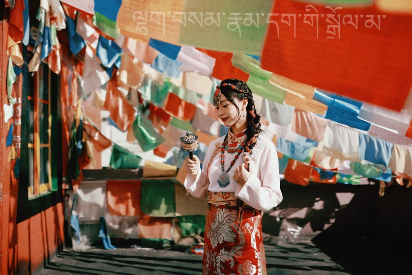 一位穿着传统服装的年轻女子站在五彩缤纷的旗帜前