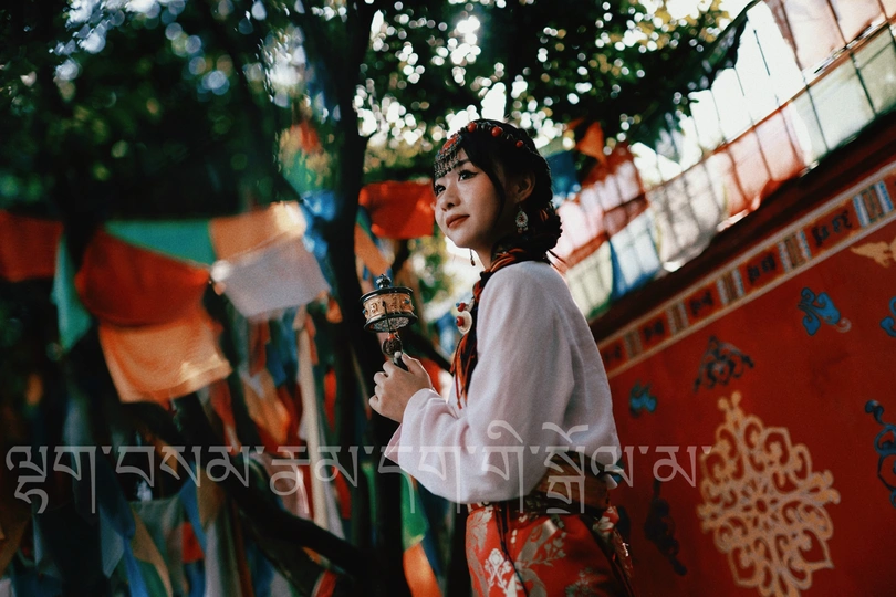 一位穿着传统服装的年轻女子手持雨伞站在一面有国旗的墙前