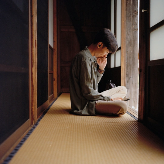 一个年轻男子坐在地板上 在一个有敞开门和窗户的房间里阅读一本书。