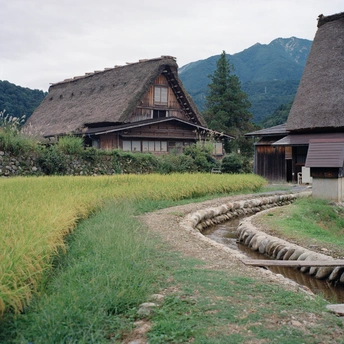 前景有一条流水 背景有一座房子 周围是草地和山。
