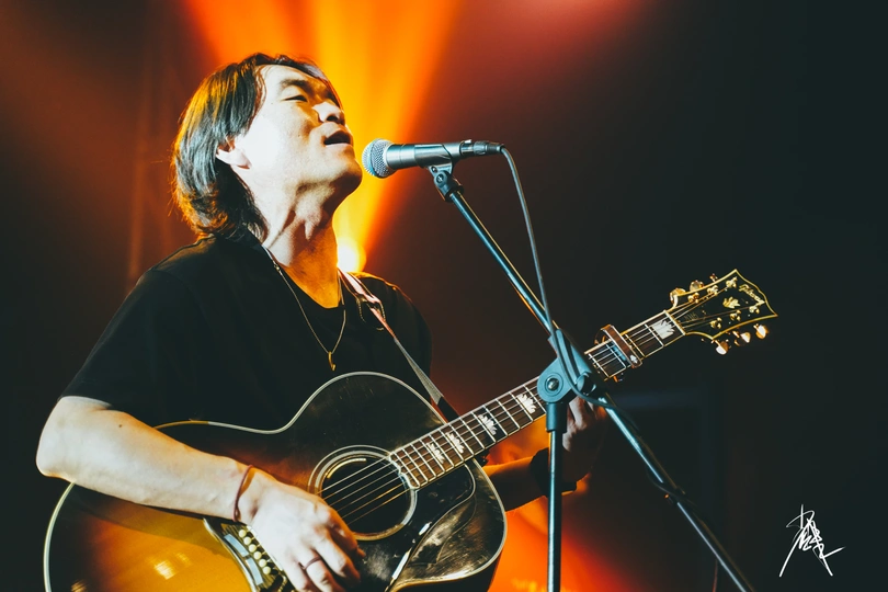 一个在音乐会或音乐节舞台上演奏乐器的人 对着麦克风唱一首歌的图像。