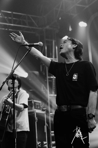 一张黑白照片 照片上是一个男人在舞台上演奏乐器 乐队在演唱会上对着麦克风唱歌。