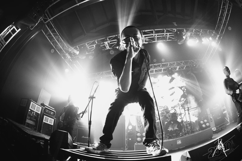 一张黑白照片 一个男子在舞台上唱歌 背景有乐队表演。