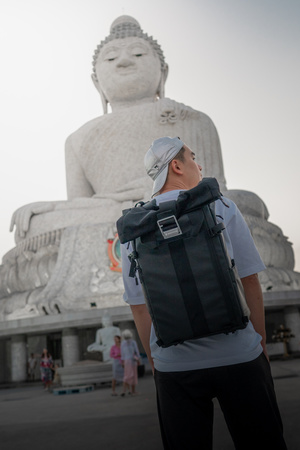 一个人站在一尊大型雕像前 背着一个背包。