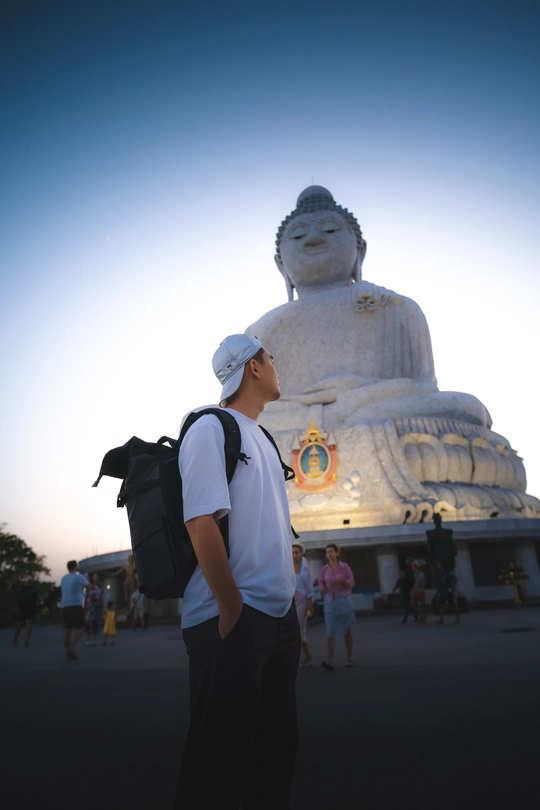 站在大型雕塑前的背着书包的年轻人