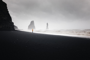一个人在黑沙滩上行走 背景是海洋和雾气
