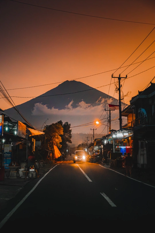 黄昏或夜晚的城市街道 路上有一辆车 天空中有一座山。