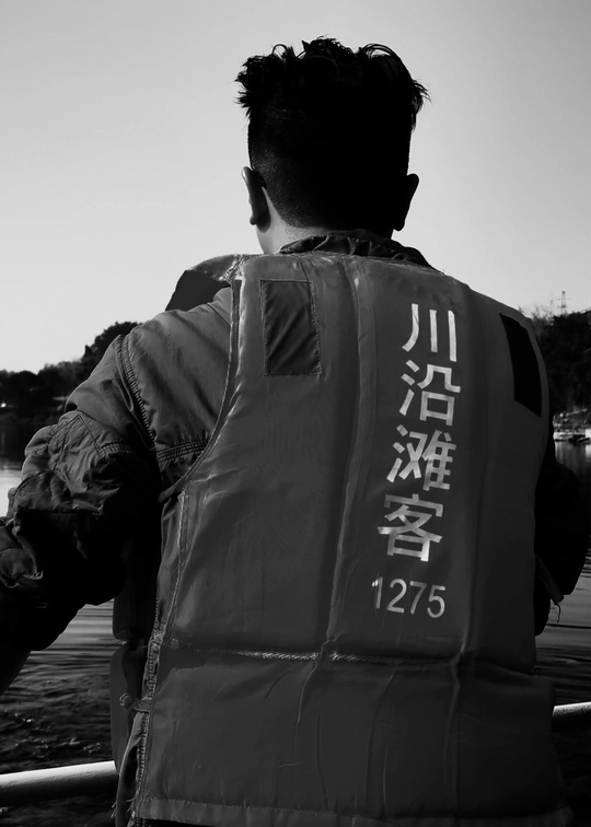 一个穿黑色背心的男子在船上看着水面 上面有亚洲文字。