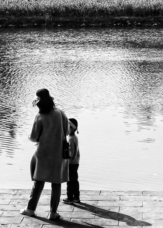 一位妇女和一名儿童站在湖或河的边缘 注视着水面。