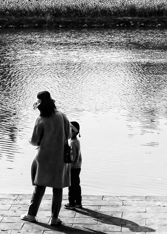 一位妇女和一名儿童站在湖或河的边缘 注视着水面。