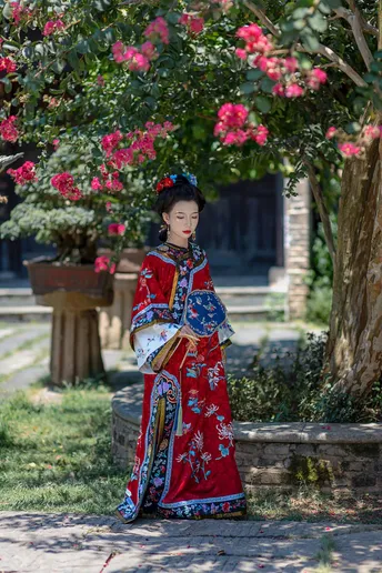 一位穿着传统裙子的年轻女子站在一朵盛开的树下