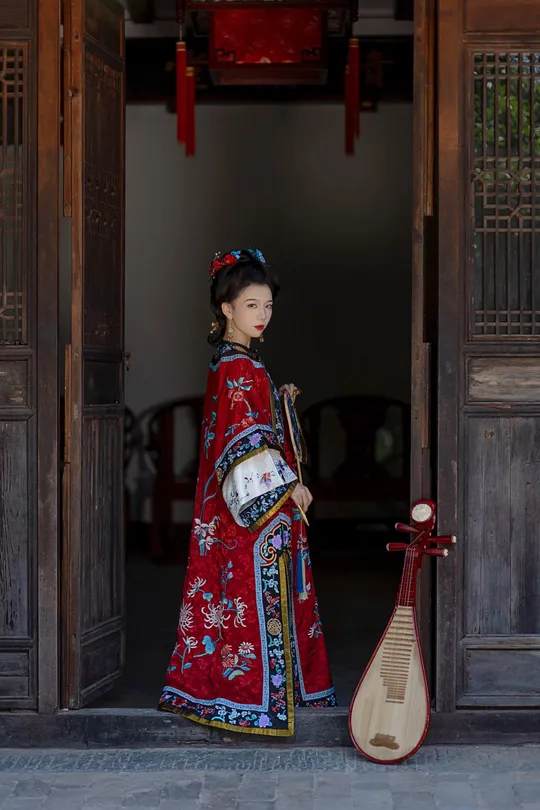 一位穿着传统红色裙子的年轻女子站在一栋建筑物的门前。