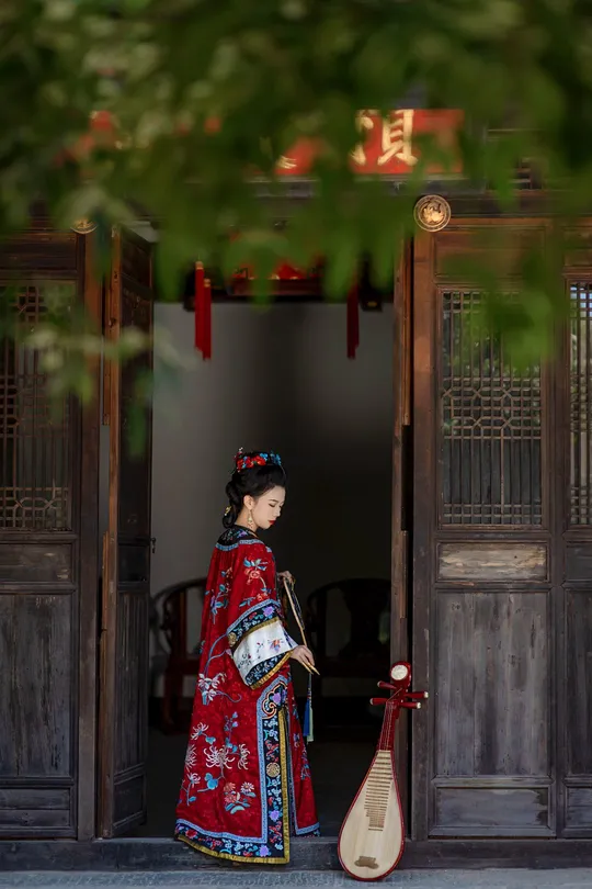一位穿着传统红色裙子的女人穿过一座老建筑的大门。