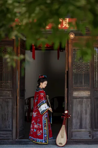 一位穿着传统红色裙子的女人穿过一座老建筑的大门。