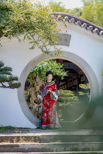 一位穿着传统红色裙子的年轻女子站在一个花园中的拱门下
