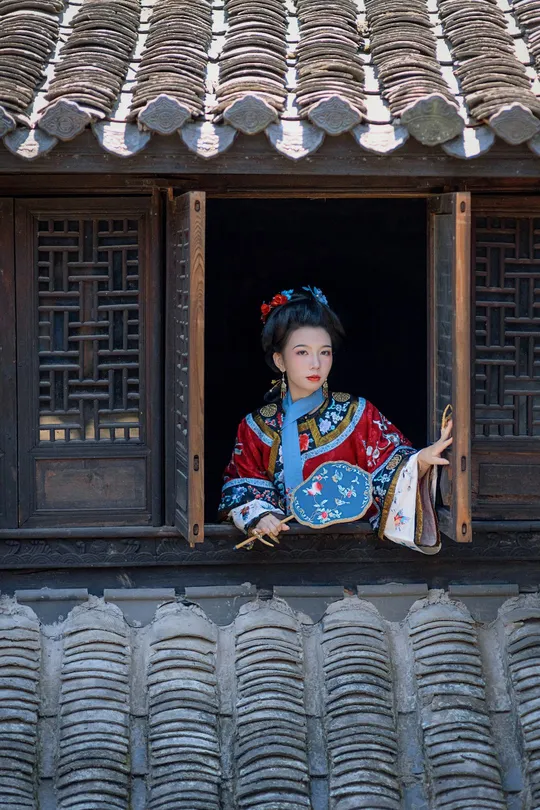 一位穿着传统服装的女人正在一栋建筑物的窗户旁向外看