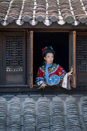 一位穿着传统服装的女人正在一栋建筑物的窗户旁向外看