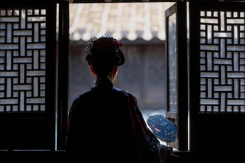 一个站在黑暗房间里的女人 正在透过窗户向外看。