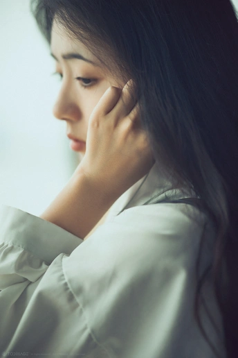 一幅身穿白衬衫的年轻女子的画像 她把手放在耳朵上 看着窗外