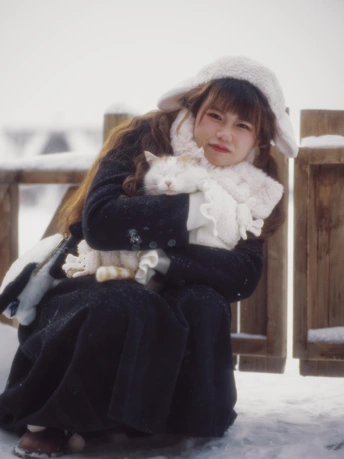 一个年轻女子抱着一只小白猫坐在雪地外面