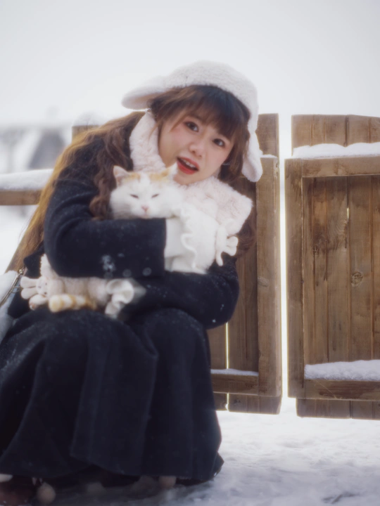 一位年轻女子抱着一只小猫坐在雪地外面