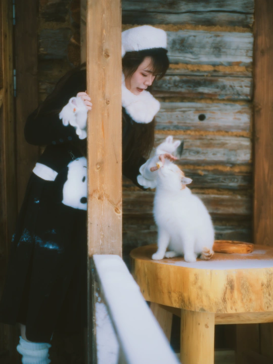 一个戴黑色连衣裙和帽子 抱着一只白色猫站在木制桌子上的女人