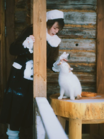 一个戴黑色连衣裙和帽子 抱着一只白色猫站在木制桌子上的女人