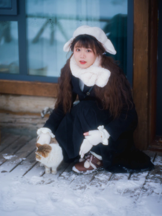 一个戴白帽子的年轻女子坐在雪中的门廊上 带着一只小白猫。