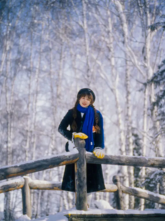 一位年轻女子站在冬天的雪中木质围栏上