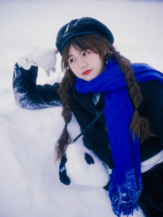 一位戴帽子和蓝色围巾的年轻女子在雪中