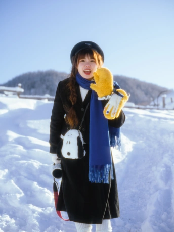 一位穿着外套、帽子、围巾和手套的年轻女子手里拿着一个毛绒玩具。