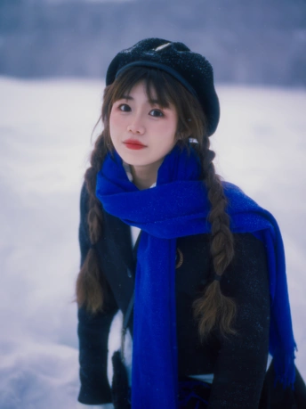 一位年轻女子戴帽子和蓝色围巾在雪中的肖像