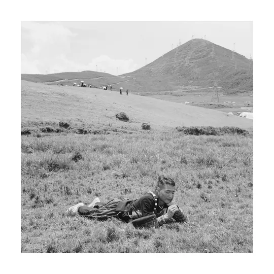 一张黑白照片 一个年轻男子坐在田野里 狗躺在草地上。