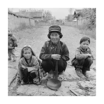 一张黑白照片 一位妇女和一名儿童坐在地上 背景中有士兵。