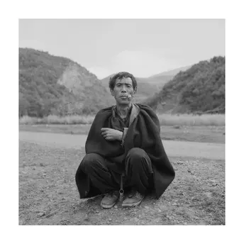 黑白照片 一位男子坐在田野中的路上 背景是山脉。