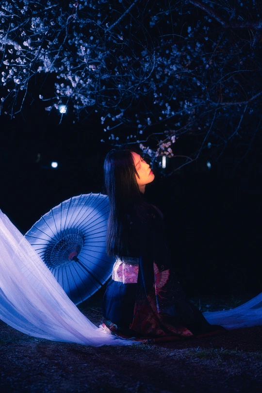 一个穿着白色连衣裙的女人拿着一把蓝色雨伞坐在树下