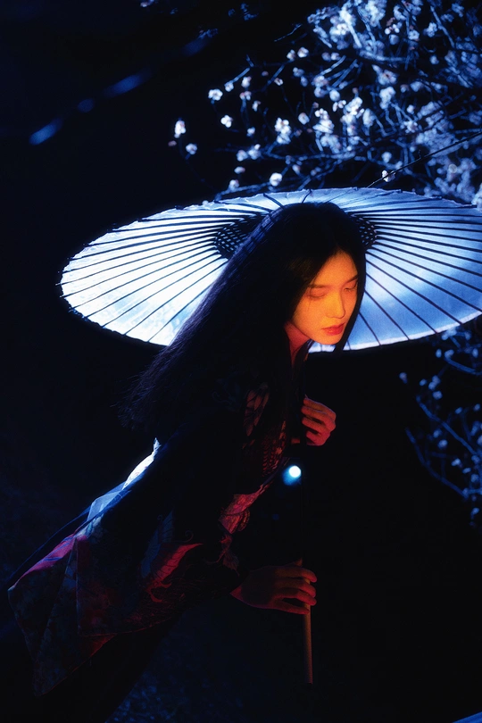 一位年轻女士拿着一把雨伞站在一棵树旁边