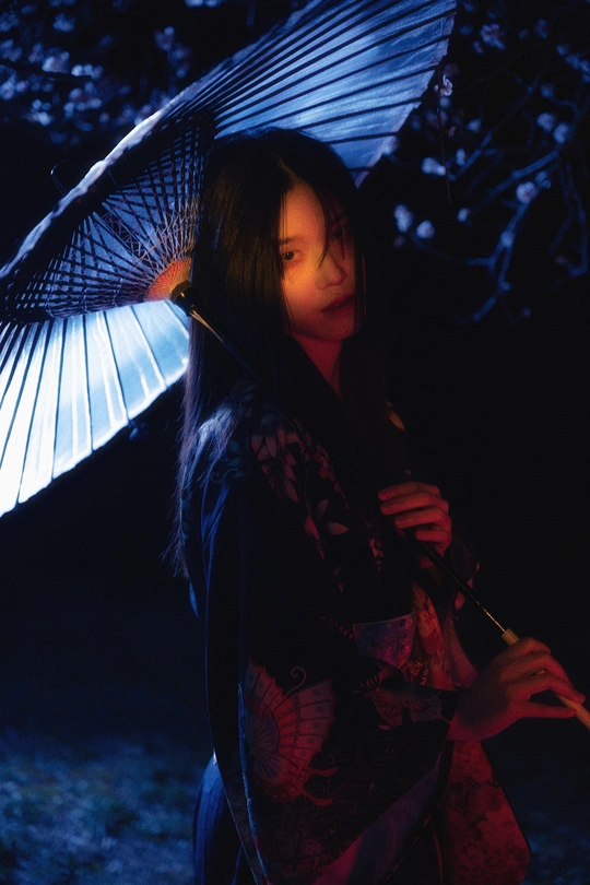 一位穿着和服的年轻女子手持蓝色雨伞站在黑暗中