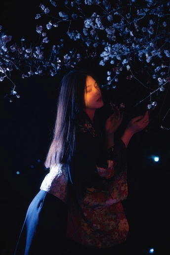 一位站在有灯光的树旁的女子手里拿着一朵花