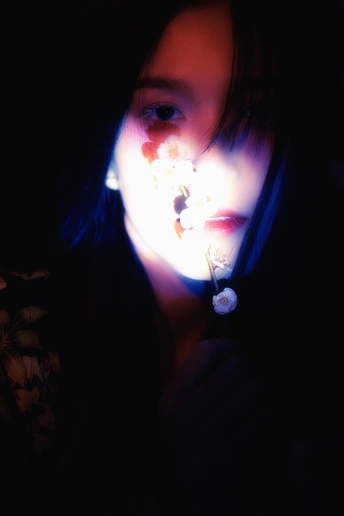 一个年轻女孩在一个黑暗的房间里举着一朵花对着自己的脸