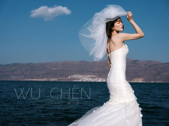 一位穿着白色婚纱的美女站在海洋中的水边 她的头纱在风中飘动。