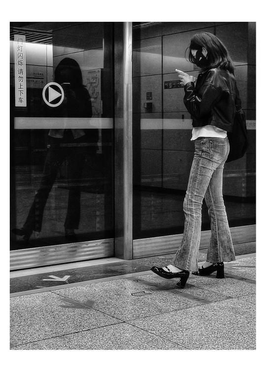 一位妇女站在人行道上 看着手机 而另一个人沿着街道走。