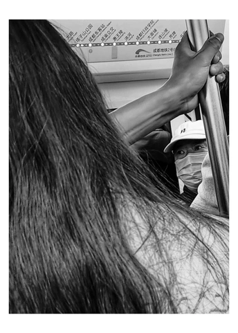 一位长发女子在乘坐公交车时 将双手背在身后。