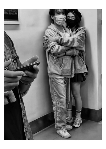 一张黑白照片 一位女士戴着口罩站在一个小女孩旁边 小女孩正在看她的手机。