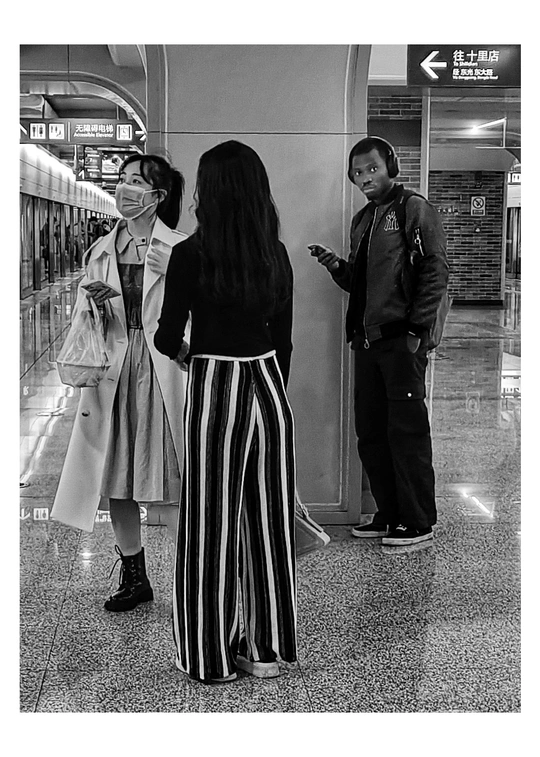 一张黑白照片 一位女士正在看她的手机 一位男士站在她旁边。