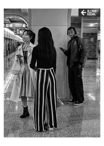 一张黑白照片 一位女士正在看她的手机 一位男士站在她旁边。