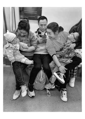 一张黑白照片 一位女士坐在地铁或火车上 正在看手机 而两个年轻女孩坐在长凳上。