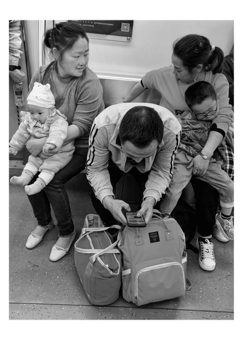 一个小男孩坐在地铁上 旁边是一个拿着行李箱的女人 其他乘客正在看着他们的行李。