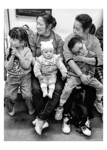 一张黑白照片 一位女性坐在地铁或火车上 抱着一个小孩子。